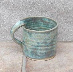 a green mug sitting on top of a cement floor