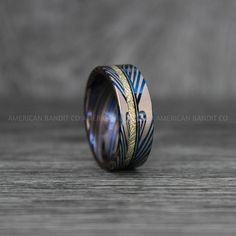 a wedding band with blue and gold inlays sits on top of a wooden table