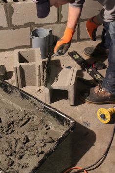 a man is pouring cement into a bucket with a hammer and other tools on the ground