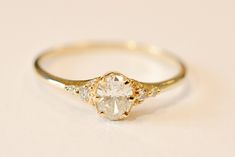 a yellow gold engagement ring with two diamonds on the band and an oval cut diamond in the center