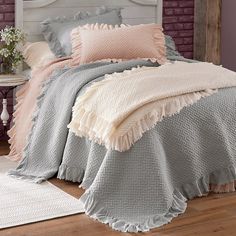 a bed with pink and grey comforters in a room next to a brick wall