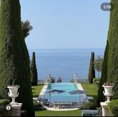 an outdoor swimming pool surrounded by tall trees and shrubs with the ocean in the background