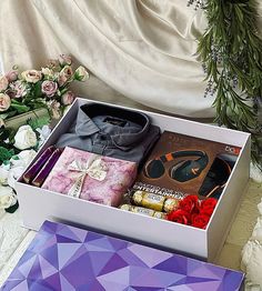 an open gift box filled with clothing, flowers and candles next to a bouquet of roses