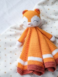 a crocheted orange and white cat laying on top of a bed next to a blanket