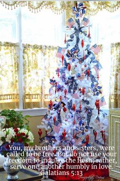 a white christmas tree decorated with red, white and blue decorations in front of a window