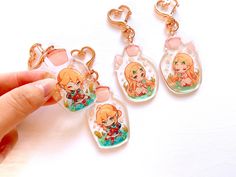 three anime keychains are being held up by someone's hand on a white surface