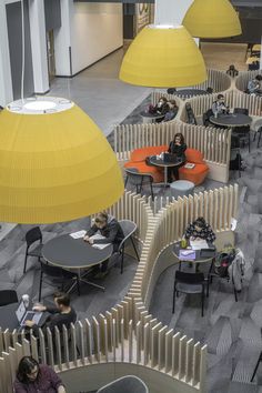 people sitting at tables in an office with yellow lamps hanging from the ceiling above them