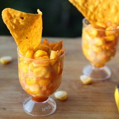 two glasses filled with corn and chips on top of a wooden table next to each other