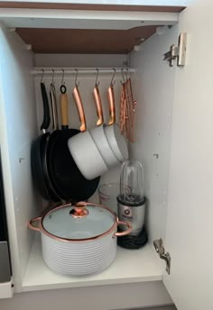 pots and pans are hanging on the wall in a cabinet with copper handles,