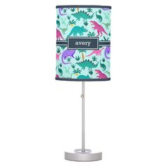 a pink and green lamp with dinosaurs on it's shade is sitting on a white stand