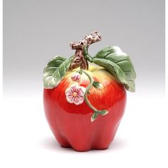 a red apple with green leaves and flowers painted on it's side, sitting in front of a gray background