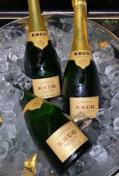 three bottles of champagne sitting on top of ice in a metal tray with gold foil