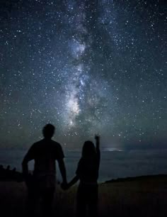 two people are standing under the stars in the sky with their hands up to each other