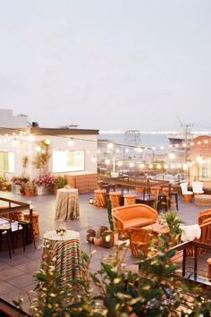 an outdoor dining area with tables and chairs on the roof terrace at night, lit by string lights