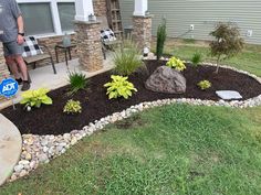 a man standing in front of a house next to a rock and grass garden area