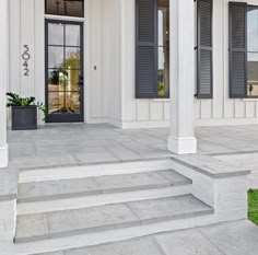 a white building with black shutters and steps leading up to the front door area