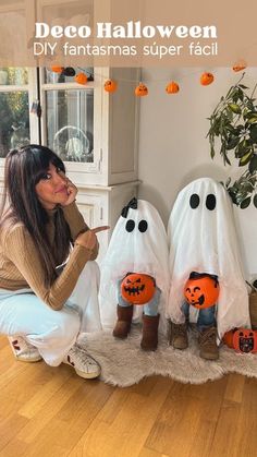 a woman sitting on the floor in front of two fake ghost heads and pumpkins