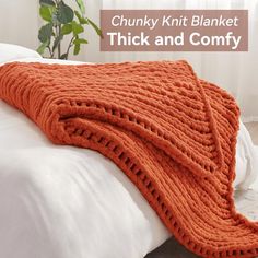 an orange knitted blanket sitting on top of a bed next to a white pillow