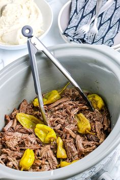 a pot roast with pickles and mashed potatoes is being stirred by tongs