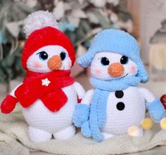 two small knitted snowmen standing next to each other on a white cloth covered surface