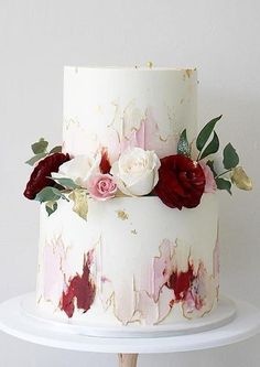 a white cake with red and pink flowers on the top is sitting on a stand