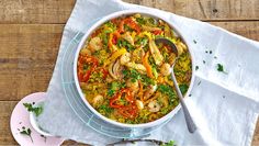 a large white bowl filled with rice and vegetables on top of a table next to a spoon