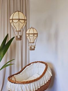 three hot air balloons hanging from the ceiling above a wicker basket with white ruffled trim