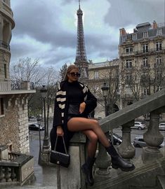 a woman sitting on top of a stone railing next to a building with the eiffel tower in the background