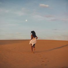 a woman is running across the desert in a white dress and headdress on