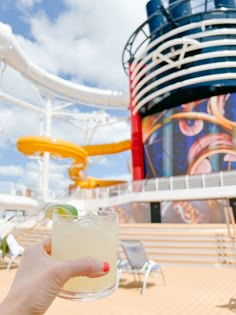 a hand holding a drink on the deck of a cruise ship