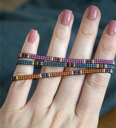 a woman's hand with three different colored beaded bracelets on her fingers