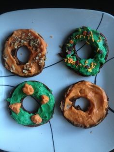 four doughnuts are arranged on a plate with sprinkles and frosting