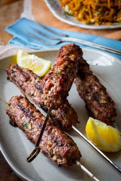 several skewers of meat on a plate with lemon wedges