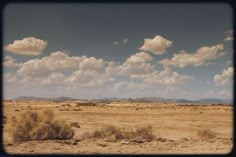 the sky is filled with fluffy clouds over an arid area in the distance are mountains