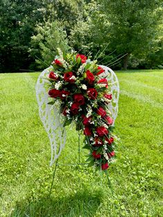 an angel's wing with red flowers and greenery on the grass in front of trees