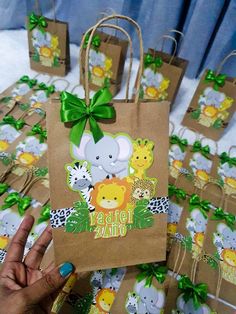 a hand holding up a brown paper bag with animals on it and green ribbon around the handle