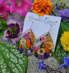 a pair of earrings with flowers on them sitting in front of purple and orange flowers