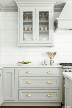 a kitchen with white cabinets and gold handles