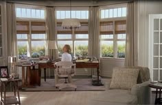 a woman is standing in the living room with her desk and chair, looking out the window