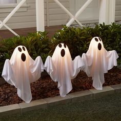 three white ghost statues in front of a house