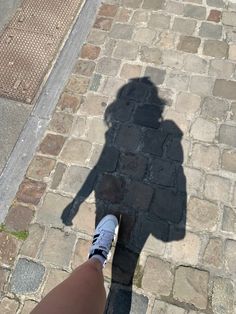 the shadow of a person standing next to a brick road with a skateboard on it