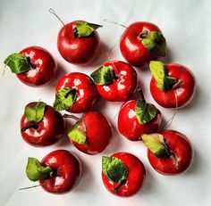 a bunch of red cherries with green leaves sitting on a white table top next to each other