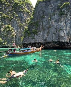 several people swimming in the water next to a boat near some mountains and cliffs,