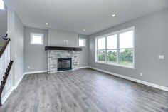 an empty living room with wood flooring and fireplace in the center, surrounded by windows