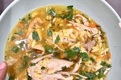 a person holding a bowl of chicken and noodle soup with parsley on top