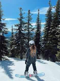 a person riding a snowboard on top of a snow covered slope with trees in the background