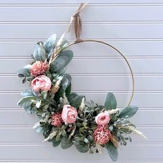 a wreath with pink flowers and greenery hanging on a wall