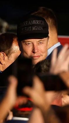 a man in a black hat is surrounded by people and taking pictures with his cell phone