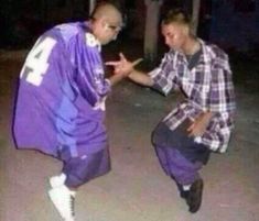 two young men are dancing together in the street at night, one is wearing an oversized purple jacket