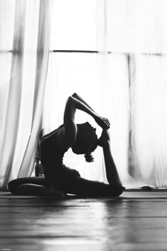 black and white photograph of a woman doing yoga in front of a window with curtains